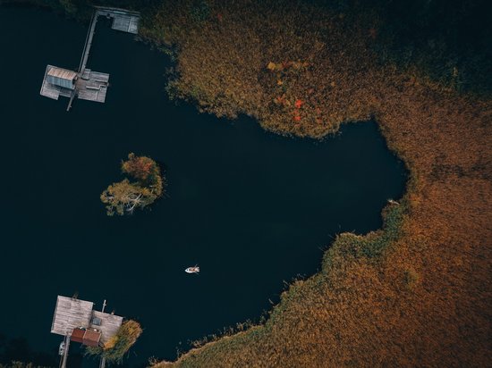 Die Dolomiten – Skiurlaub und so viel mehr Luftaufnahme eines dunklen Sees mit Stegen, Insel und Boot