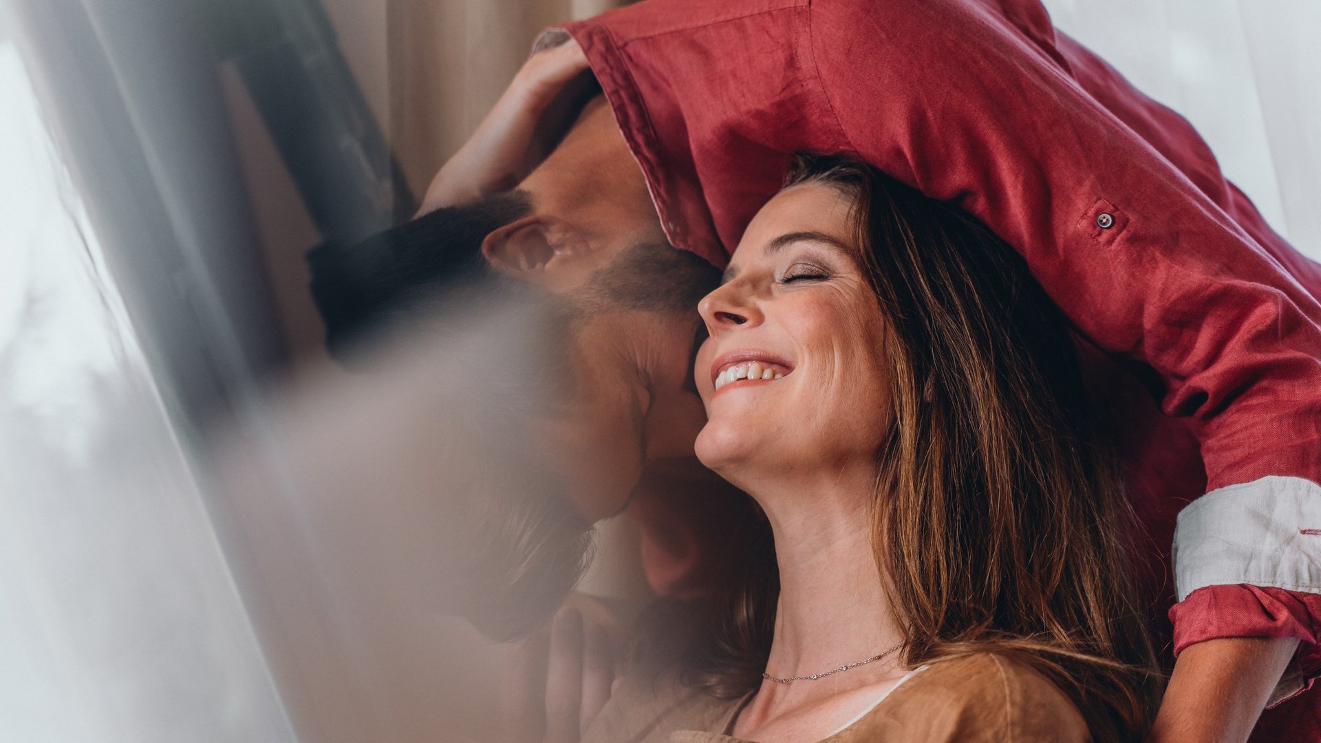 Silvester in den Bergen Glückliches Paar umarmt sich nah an einem Fenster mit Vorhängen