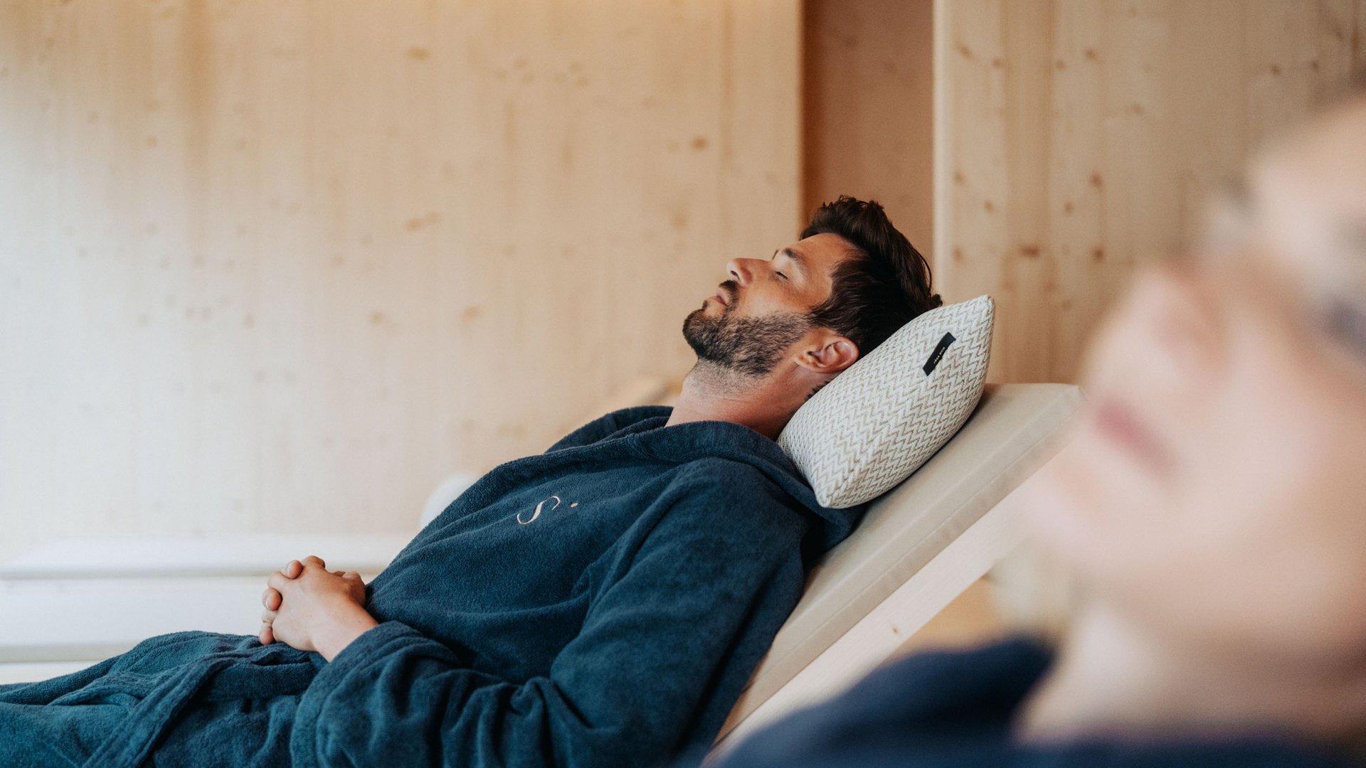 Day Spa in Südtirol – Wellness für die Seele Mann entspannt auf Liegestuhl mit geschlossen Augen und Kissen im Spa