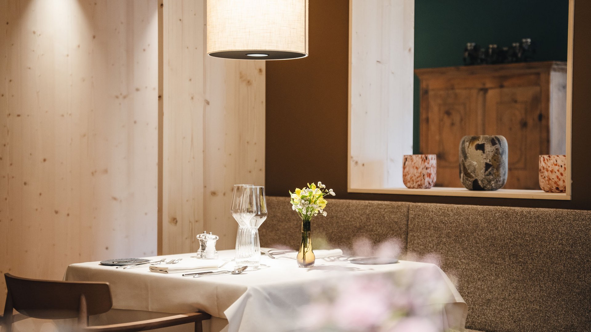 Südtiroler Rezepte. Neu interpretiert. Gemütlicher Restauranttisch mit weißer Tischdecke und Blumenvase