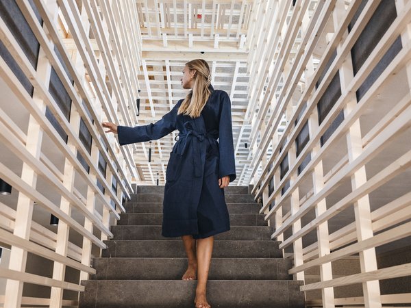 Wellness Aphrodite: Sensoria Dolomites unter den Siegern Frau in blauem Bademantel geht barfuß eine Treppe in modernem Holzrahmenhaus hinauf