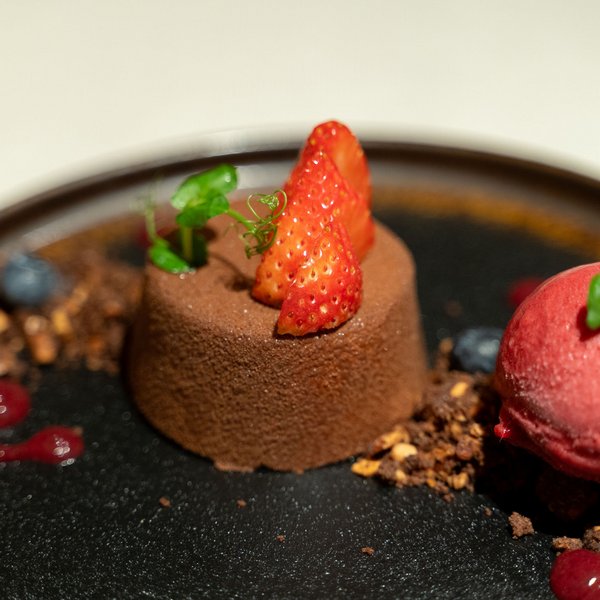 Genussurlaub in Südtirol – Sensoria Dolomites Schokoladendessert mit Erdbeeren und rotem Sorbet auf schwarzem Teller