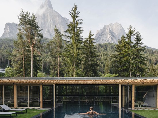 Wellnesshotel auf der Seiser Alm – Luxus für die Seele Frau im Pool vor Holzgebäude mit Bergen und Bäumen im Hintergrund