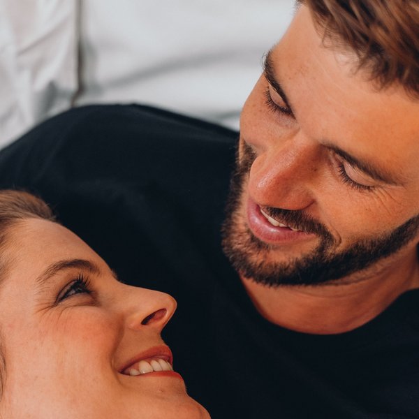Romantischer Kurzurlaub für Verliebte – Sensoria Dolomites Junges Paar liegt im Bett und lächelt sich liebevoll an
