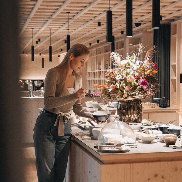 Genussurlaub in Südtirol – Sensoria Dolomites Frau nimmt Essen vom Buffet in modernem Restaurant