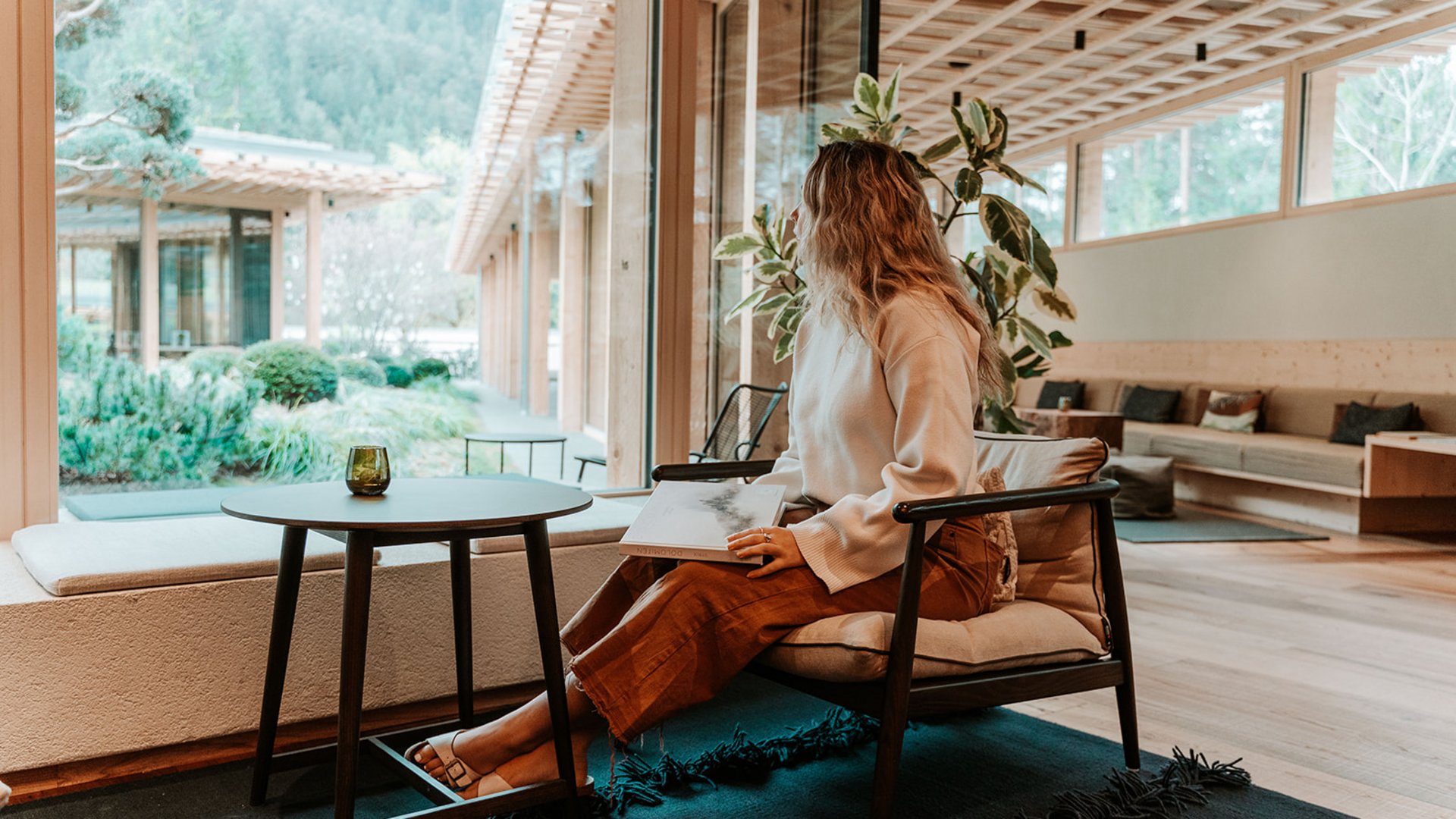 Inclusive services – last-minute South Tyrol holidays Woman sitting with book in modern room looking out large window at garden