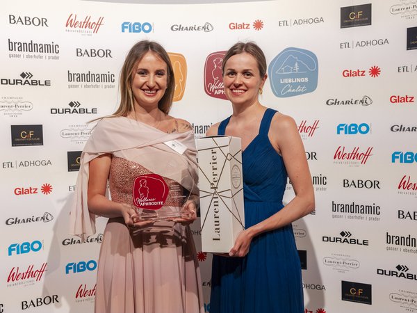 Wellness Aphrodite: Sensoria Dolomites unter den Siegern Zwei Frauen halten Preis und Geschenk vor Sponsorenwand