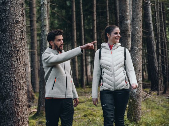 Die Dolomiten – Skiurlaub und so viel mehr Zwei Personen wandern im Wald, Mann zeigt auf etwas, Frau lächelt