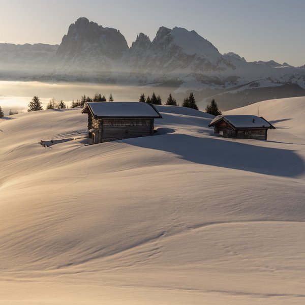 Seiser Alm: Skiurlaub de luxe Verschneite Hütte vor Bergen bei Sonnenaufgang