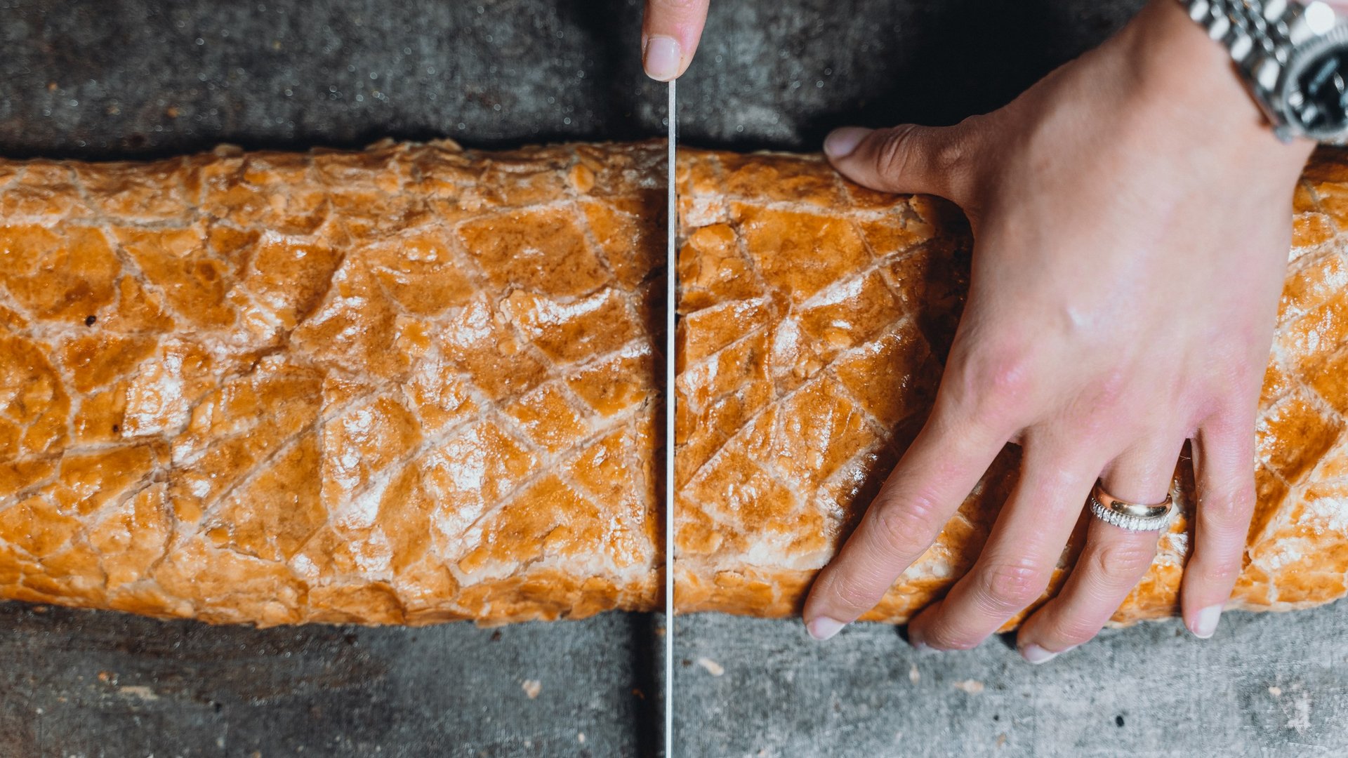 Unser Genussmarkt – perfekt für Ihr Romantikwochenende Hand schneidet frisches Baguette mit einem Messer