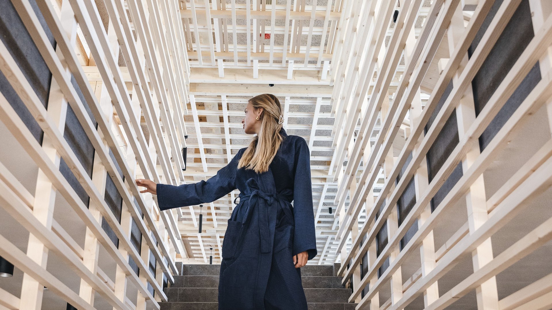 Wellness Aphrodite: Sensoria Dolomites unter den Siegern Frau in Bademantel geht barfuß eine Treppe mit Holzgittern hinunter