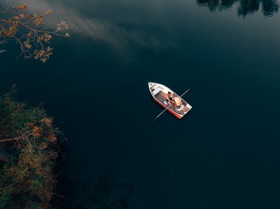 Hotel in Seis am Schlern gesucht? Sensoria Dolomites gefunden! Zwei Personen sitzen in einem Boot auf ruhigem Wasser nahe Uferbewuchs