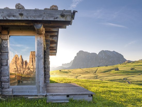 Ein Sommerurlaub in den Bergen Berghütte mit Fensterspiegelung der Dolomiten und grüner Wiese im Sonnenlicht