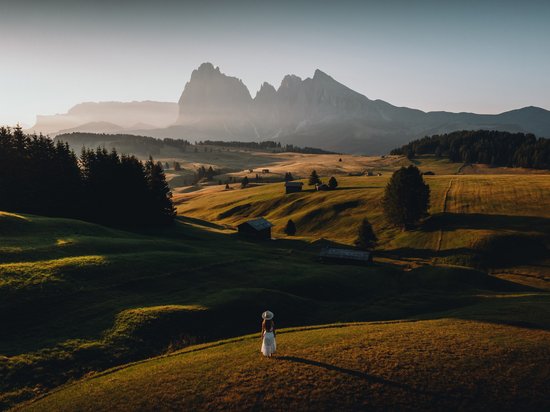 Hotel in Seis am Schlern gesucht? Sensoria Dolomites gefunden! Frau im weißen Kleid auf einer Wiese mit Bergpanorama im Hintergrund