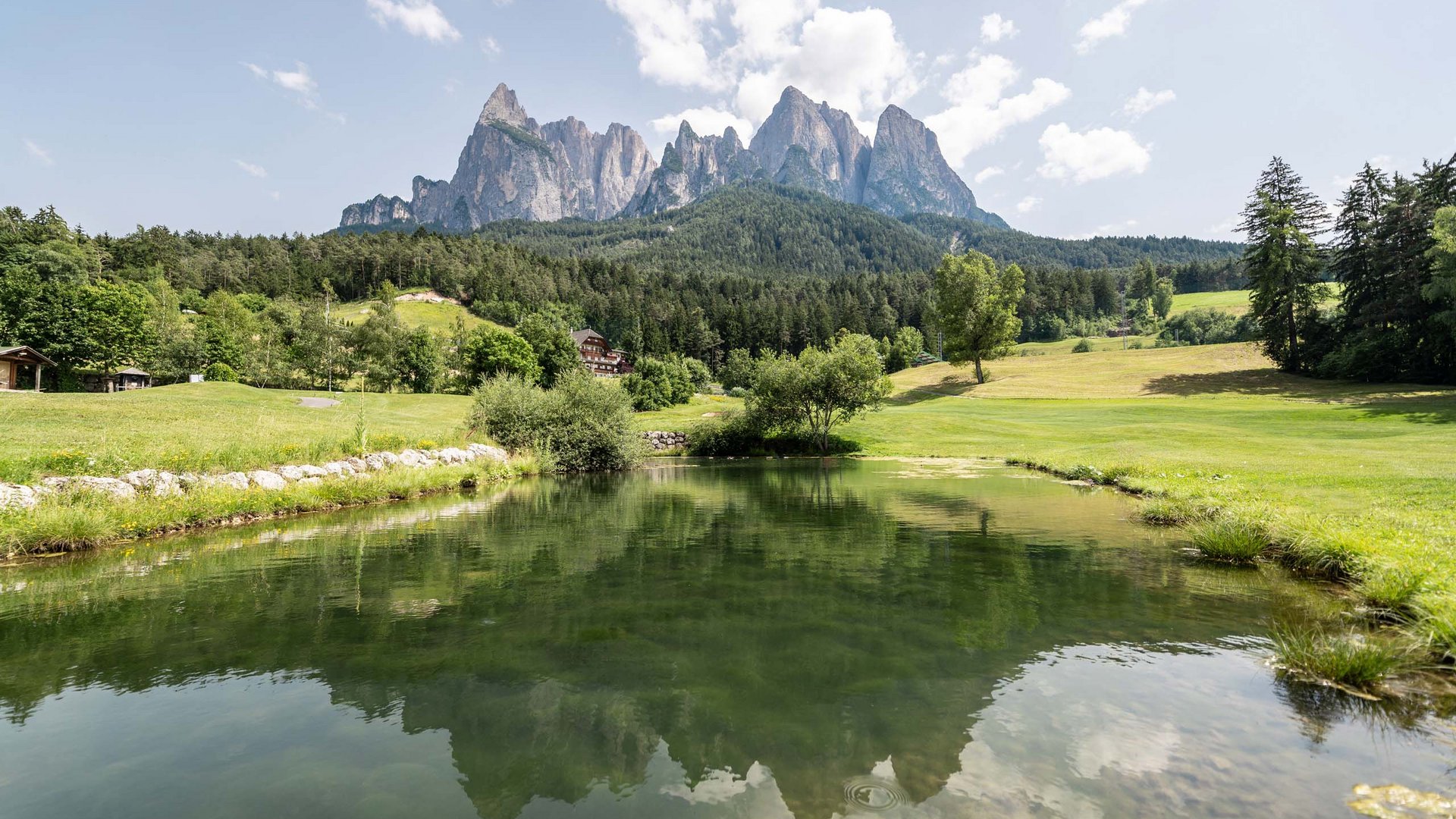 Golf und Wellness – Ihr Golfhotel nahe der Seiser Alm Berglandschaft mit See und bewaldeten Hügeln unter blauem Himmel