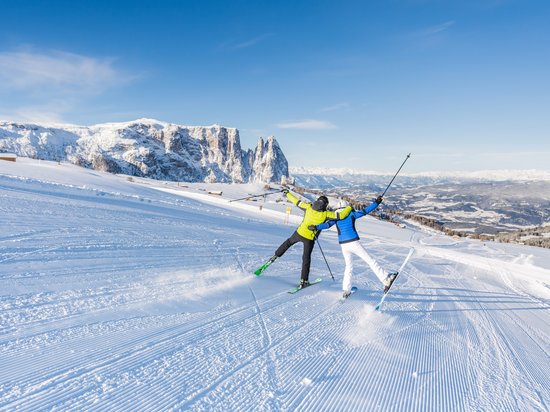 Mehr als ein Hotel auf der Seiser Alm: Sensoria Dolomites Zwei Skifahrer in bunten Jacken fahren auf verschneiter Piste mit Bergkulisse