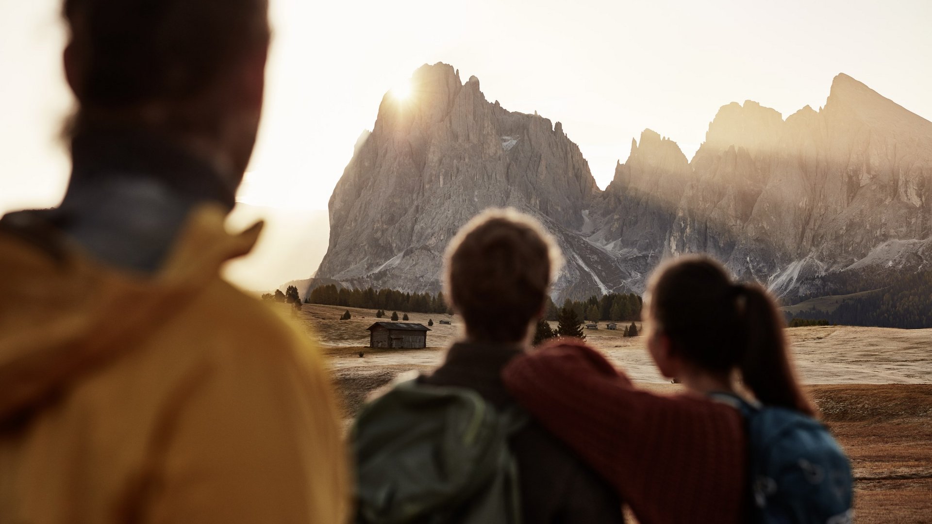 Ein Sommerurlaub in den Bergen Drei Menschen schauen auf die Berge bei Sonnenuntergang auf einer Wiese mit einer Hütte