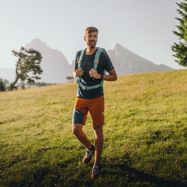 Aktivurlaub in Südtirol – bereit für Natur pur? Mann mit Rucksack wandert in einer grünen Bergwiese bei Sonnenschein