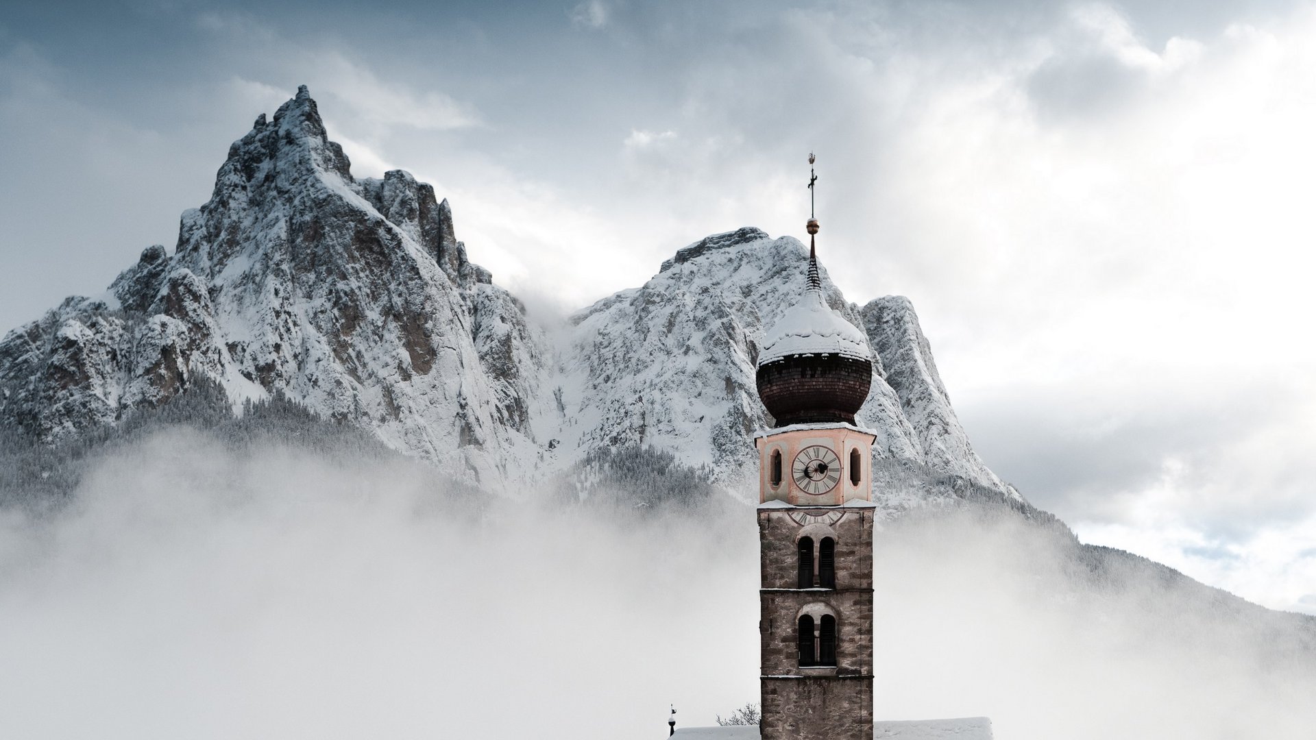 Seiser Alm: Skiurlaub de luxe alte Kirche im Schnee vor nebligen, schneebedeckten Bergen
