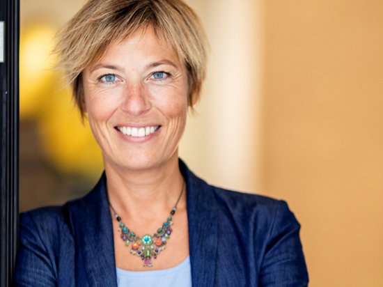 My Olympic Mindset Retreat 2026 Frau in blauem Blazer lächelt selbstbewusst mit verschränkten Armen