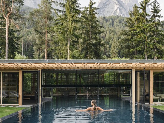 Luxus für die Seele im Kurzurlaub in Südtirol Frau im Pool mit Blick auf bewaldete Berge und moderne Gebäude