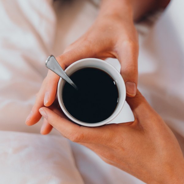 Romantischer Kurzurlaub für Verliebte – Sensoria Dolomites Hände halten eine Tasse schwarzen Kaffee mit Löffel im Bett