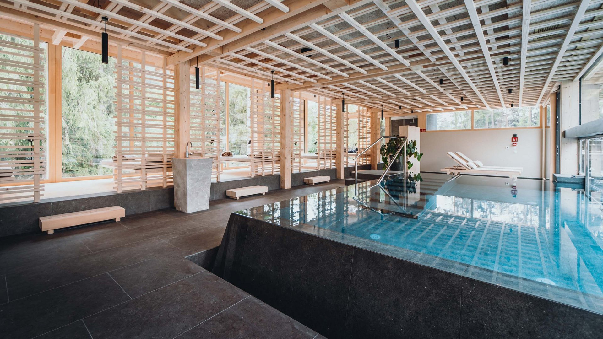 Day Spa in Südtirol – Wellness für die Seele Moderner Innenpool mit Holzdecke und Liegestühlen neben großen Fenstern