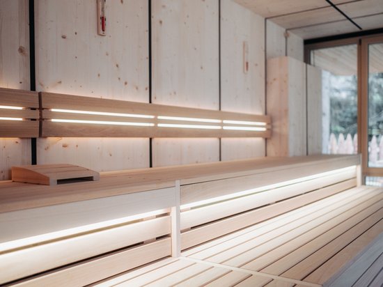 Das Badehaus im Hotel mit Pool in den Dolomiten Innenansicht einer modernen Sauna mit Holz- und indirekter Beleuchtung