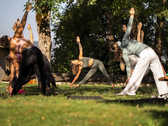Seiser Alm Balance – im Einklang mit der Natur Gruppe macht Yoga-Übungen im Freien auf einer Wiese unter Bäumen