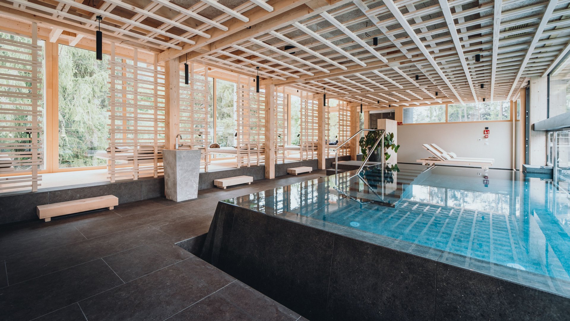 Das Badehaus im Hotel mit Pool in den Dolomiten Moderner Innenpool in stilvollem Holz- und Steindesign mit Liegestühlen
