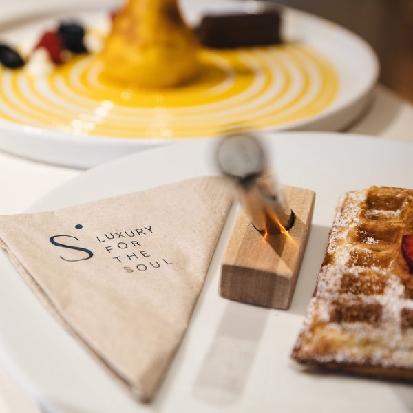 Genussurlaub in Südtirol – Sensoria Dolomites Serviette mit Aufdruck Luxury for the Soul neben Waffel und Dessert auf Teller