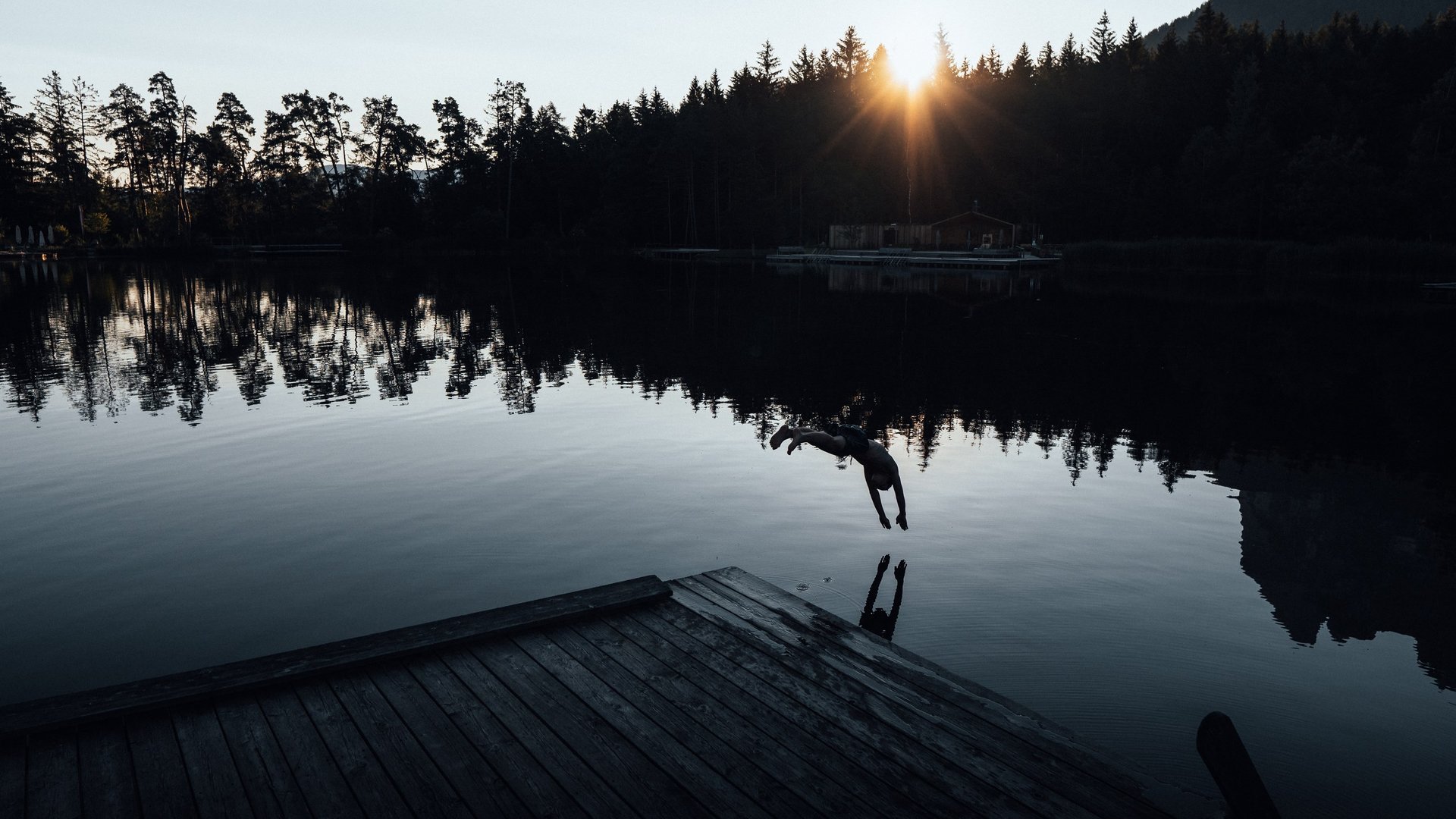 Kraftorte in Südtirol Person beim Sprung ins Wasser am See mit Sonnenuntergang und Wald im Hintergrund