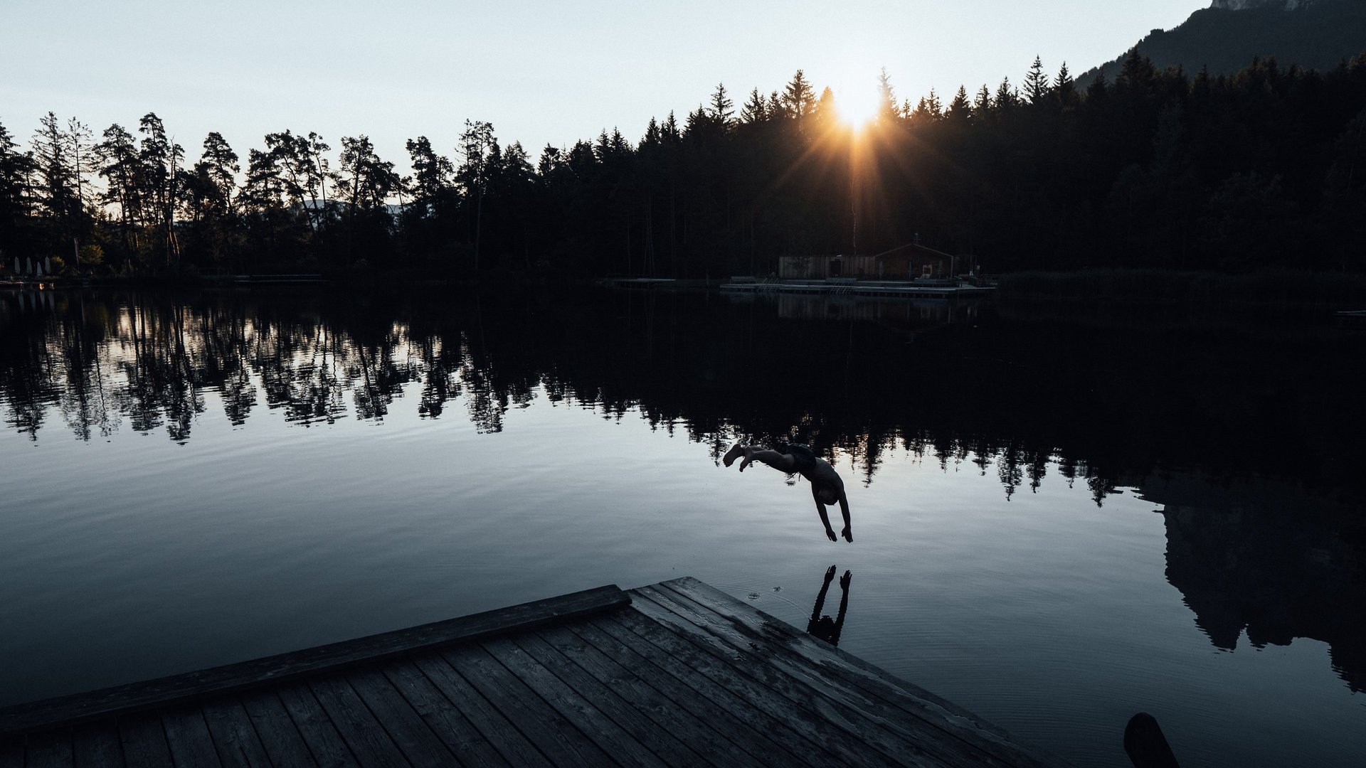 Größte Hochalm Europas – ein Kraftplatz mit Seele Person beim Sprung ins Wasser am See mit Sonnenuntergang und Wald im Hintergrund