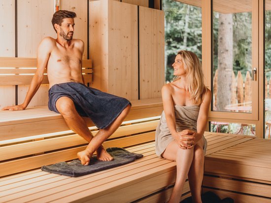 Wellnesshotel auf der Seiser Alm – Luxus für die Seele Mann und Frau entspannen in einer Holzsauna mit Fenster und Blick ins Grüne