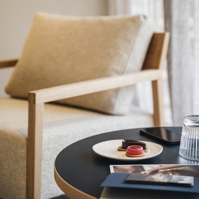 Essence West Beistelltisch mit Keksen, Glas und Handy vor einem beigen Sessel