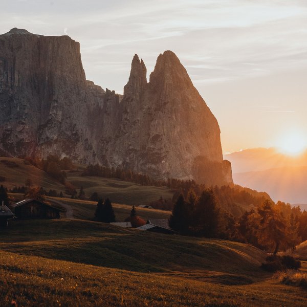 Aktivurlaub in Südtirol – bereit für Natur pur? Sonnenaufgang über grasbewachsenem Hügel mit markantem Felsen in den Dolomiten