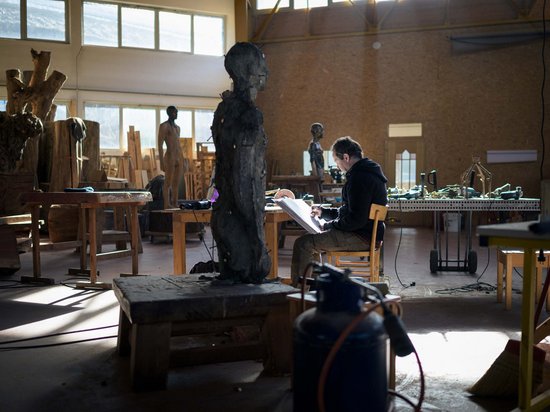 Sensoria Art Edition 01 Künstler zeichnet in Atelier mit hölzernen Skulpturen und Werkzeugen