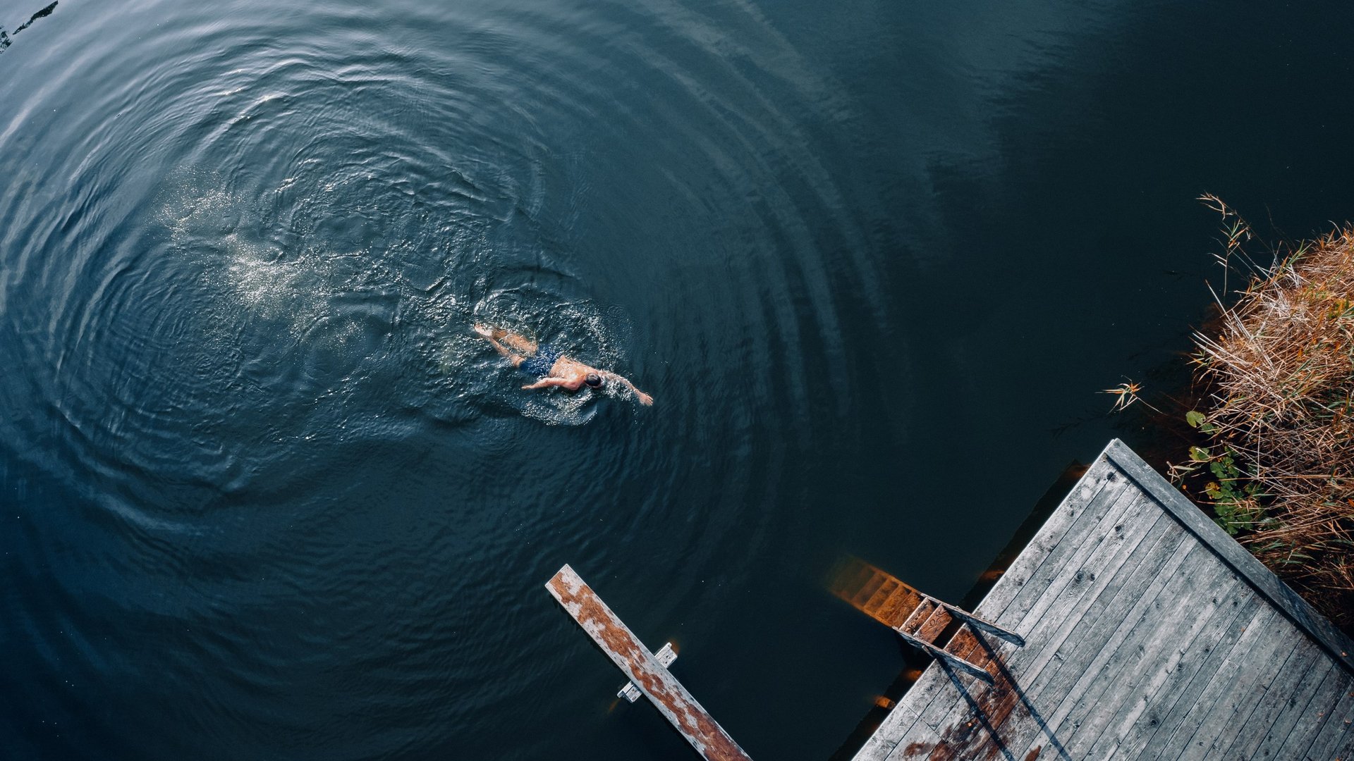 Erholung in und mit der Natur – Ihr Spa-Hotel in Südtirol Person schwimmt im dunklen Wasser neben altem Holzsteg