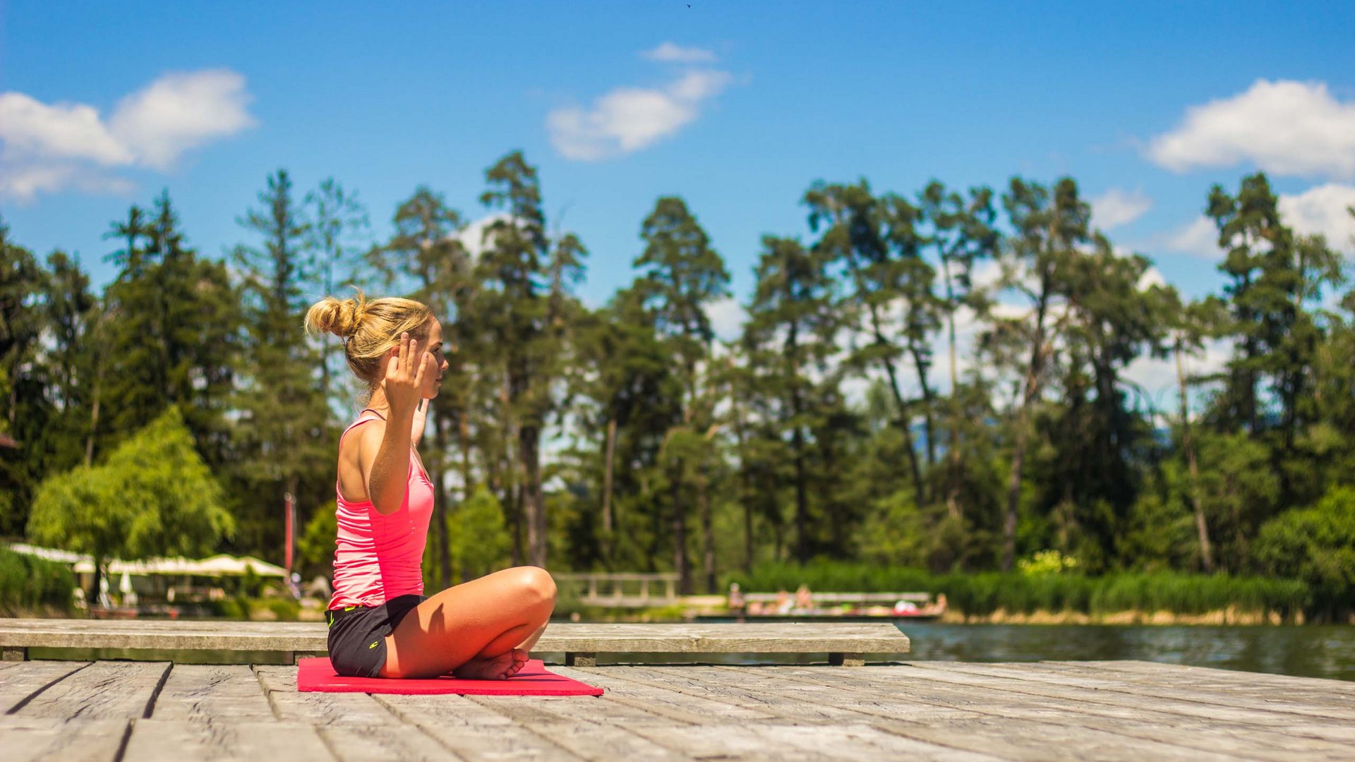 Luxus für die Seele: Ihr Yogahotel in Südtirol Frau meditiert auf roter Matte am Seeufer bei sonnigem Wetter