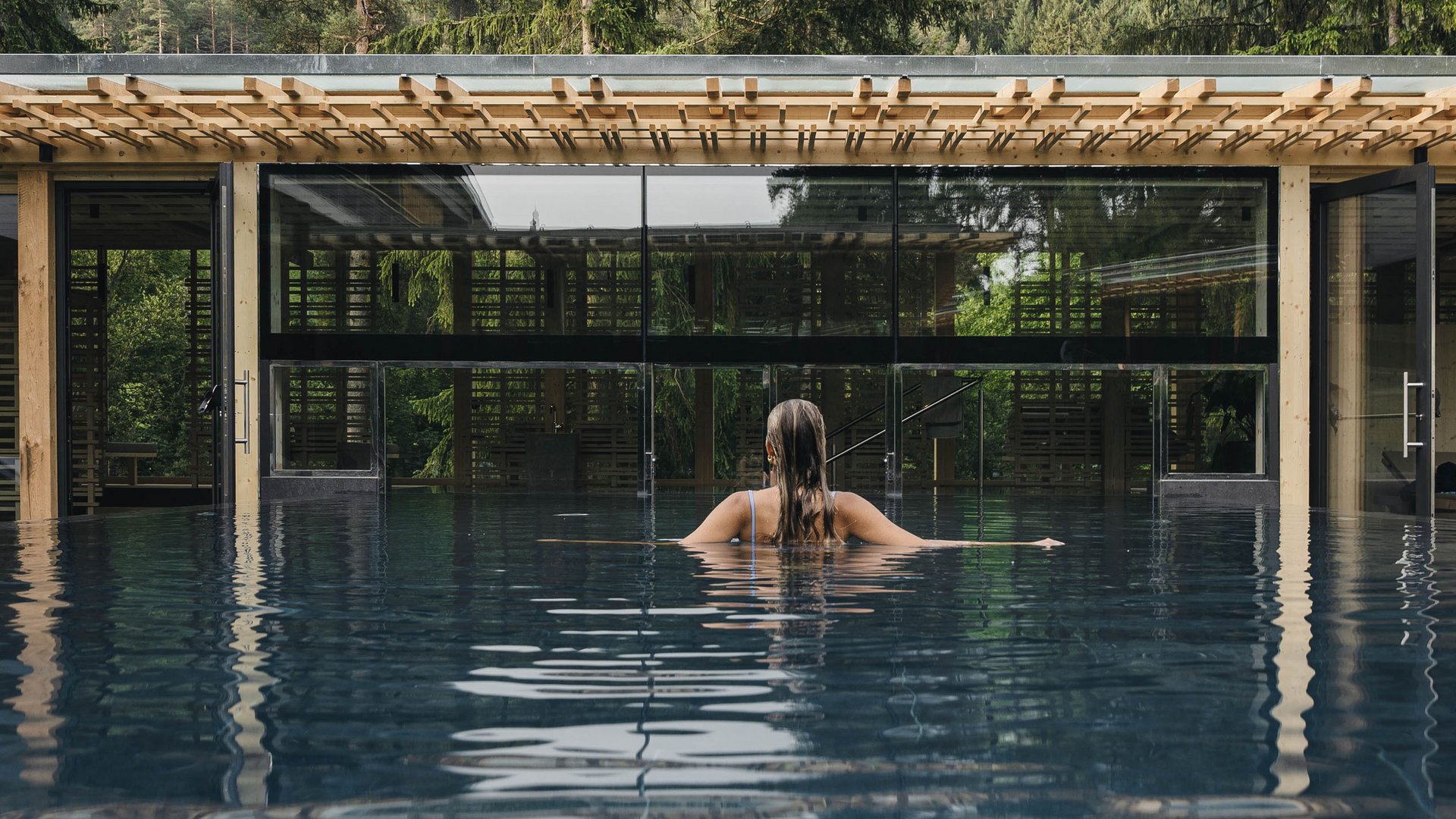 Wellness Aphrodite: Sensoria Dolomites unter den Siegern Frau im Pool vor Glasgebäude und Berglandschaft mit Bäumen