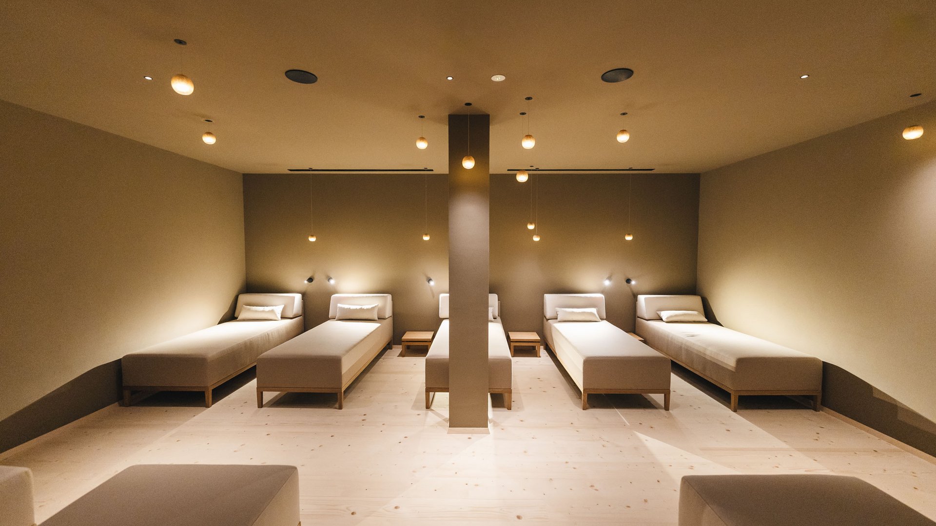 Day Spa in Südtirol – Wellness für die Seele Modernes Ruheraum mit mehreren weißen Liegen und warmen Deckenleuchten