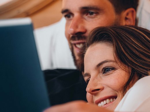 Inclusive services – last-minute South Tyrol holidays Couple lying together smiling while looking at a laptop
