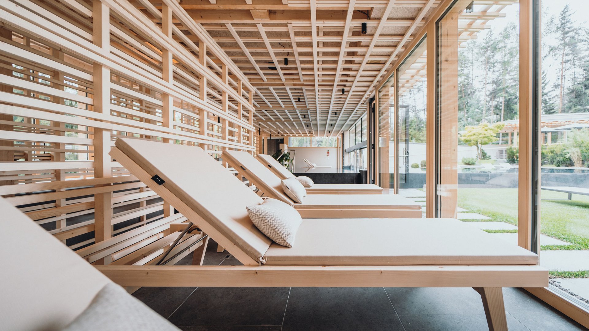 Das Badehaus im Hotel mit Pool in den Dolomiten Moderne Liegestühle im Wellnessbereich mit großem Fenster zum Garten