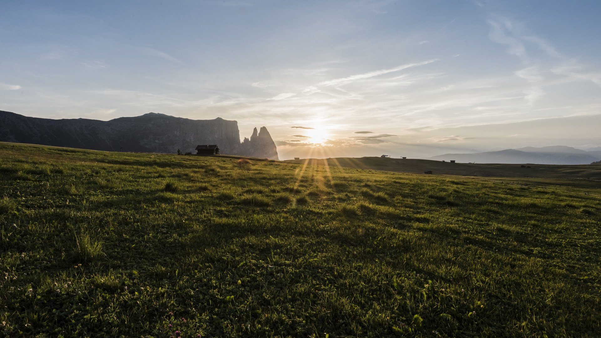 Mehr als ein Hotel im Naturpark Schlern-Rosengarten Sonnenuntergang über einer weiten grünen Wiese mit Bergen im Hintergrund