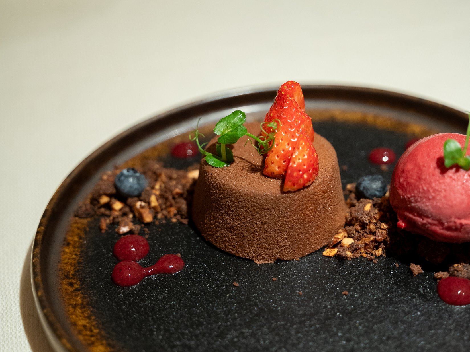 Momente, die bleiben. Im Luxushotel auf der Seiser Alm. Schokoladendessert mit Erdbeere, Beeren und Sorbet auf braun-schwarzem Teller