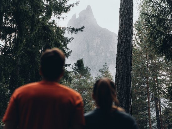Mehr als ein Hotel im Naturpark Schlern-Rosengarten Zwei Personen schauen im Wald auf einen hohen Berggipfel