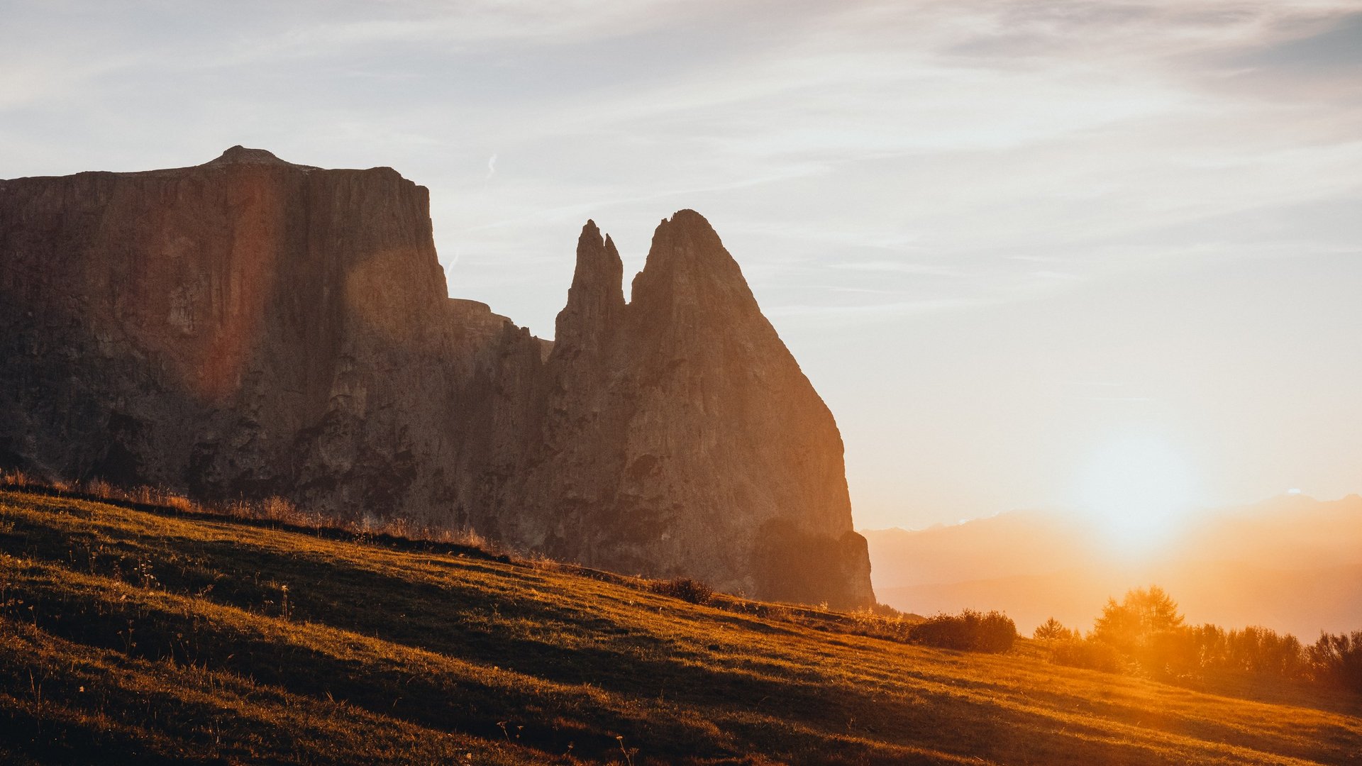Urlaub in den Dolomiten – Urlaub im Sensoria Dolomites Sonnenuntergang über Bergen und Grasland mit orangefarbenem Licht