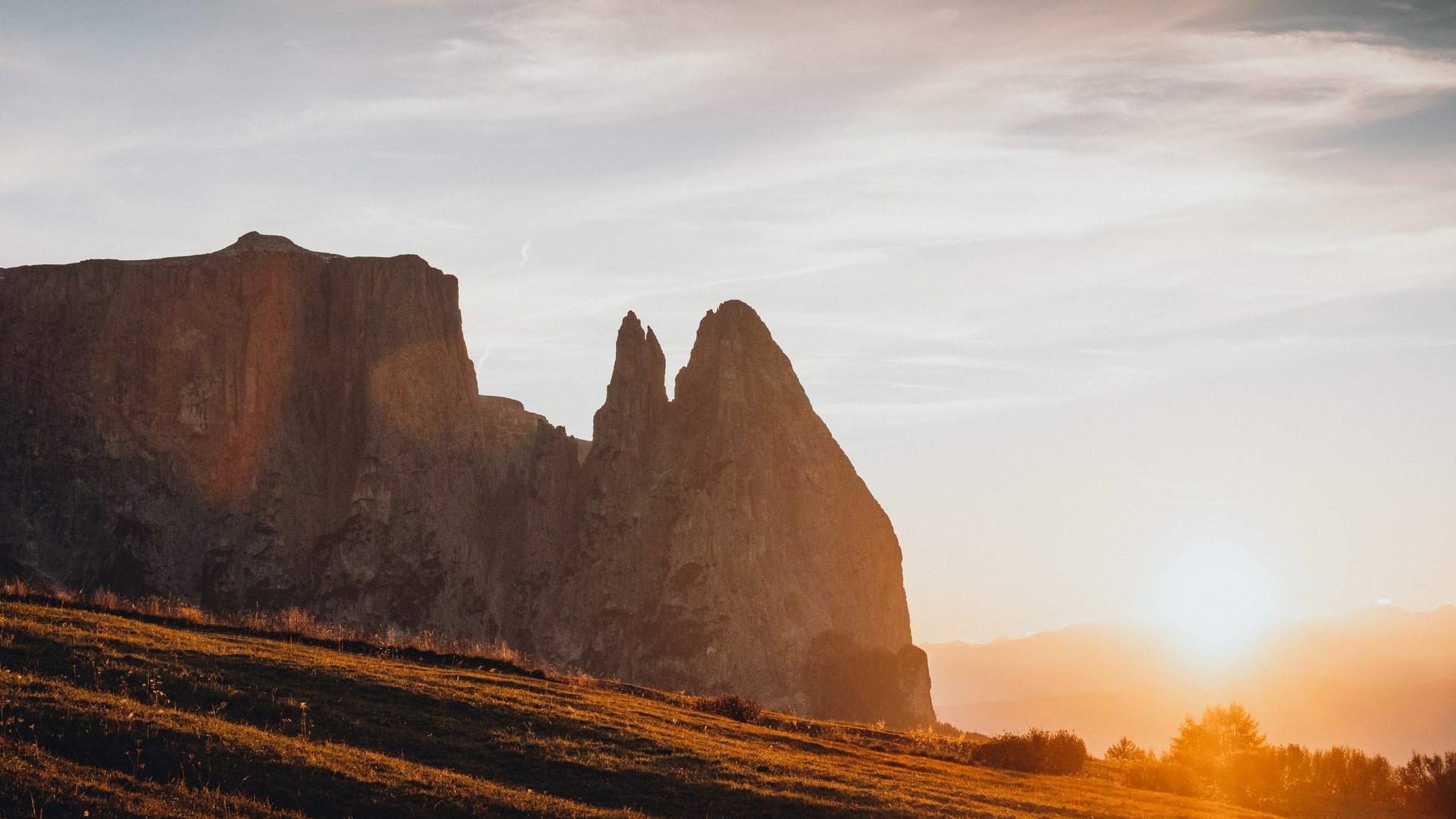 Mehr als ein Hotel im Naturpark Schlern-Rosengarten Sonnenuntergang über Bergen und Grasland mit orangefarbenem Licht