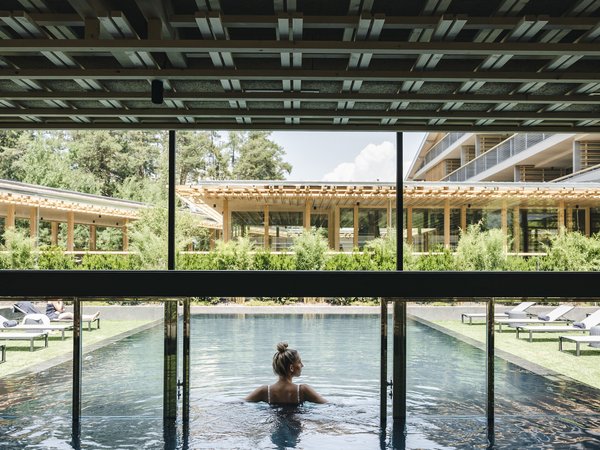 Wellness Aphrodite: Sensoria Dolomites unter den Siegern Frau steht im Hotel-Außenpool mit moderner Holzarchitektur im Hintergrund
