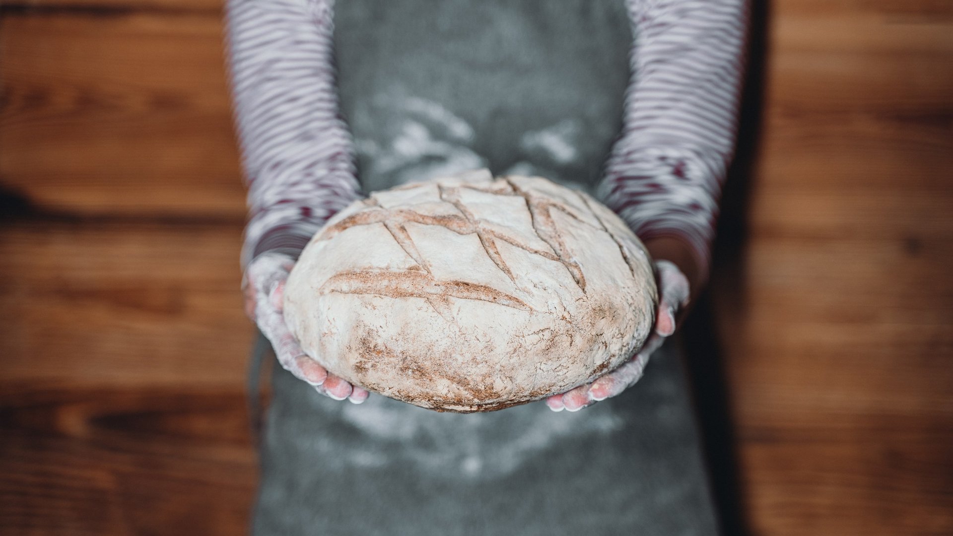 Unser Genussmarkt – perfekt für Ihr Romantikwochenende Person hält ein rundes, frisch gebackenes Brot mit Mehl bedeckte Hände